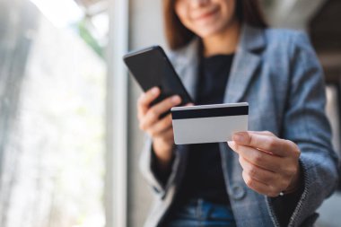 Güzel bir Asyalı kadın cep telefonundan alışveriş yapmak için kredi kartı kullanıyor.