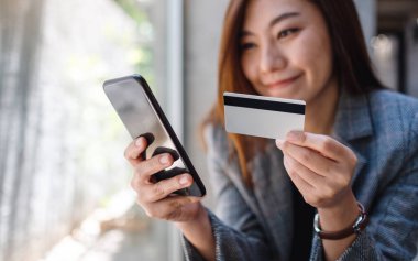 Güzel bir Asyalı kadın cep telefonundan alışveriş yapmak için kredi kartı kullanıyor.