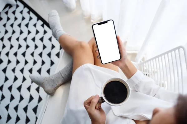 ベッドルームでコーヒーを飲みながら 白いデスクトップ画面と携帯電話を保持している女性のトップビューモックアップイメージ — ストック写真