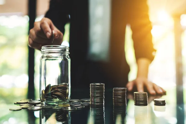 お金と金融の概念を節約するためにテーブルの上にコインスタックとガラス瓶にコインを入れてビジネスマンの女性のクローズアップイメージ — ストック写真