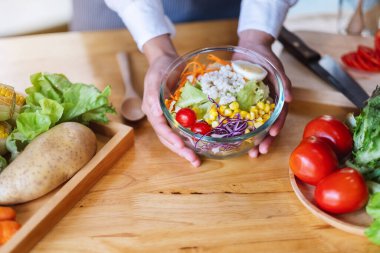 Mutfakta bir kase taze sebze salatası ve yemek pişiren bir kadın şefin yakın plan görüntüsü.