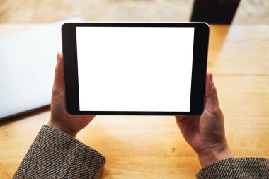 Masada dizüstü bilgisayarlı, boş beyaz masaüstü ekranlı, elinde siyah tablet bilgisayar tutan bir kadının en üstteki görüntüsü 