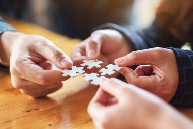 Beyaz yapboz parçalarını bir araya getirip bir araya getiren bir grup insanın yakın plan görüntüsü.