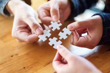 Beyaz yapboz parçalarını bir araya getirip bir araya getiren bir grup insanın yakın plan görüntüsü.