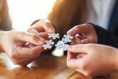 Beyaz yapboz parçalarını bir araya getirip bir araya getiren bir grup insanın yakın plan görüntüsü.