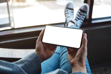 Kafede otururken elinde boş beyaz masaüstü ekran olan cep telefonu tutan bir kadının görüntüsü