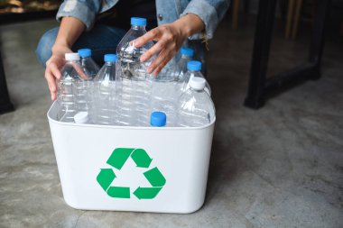 Geri dönüşümlü çöp şişelerini toplayıp evdeki çöp kutusuna koyan bir kadın.