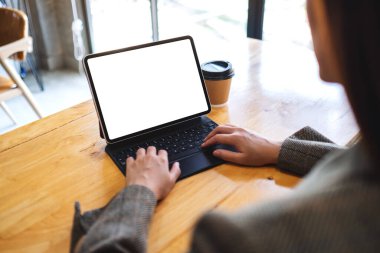 Tablet klavyesinde boş beyaz masaüstü ekran ve masada kahve fincanı olan bilgisayar bilgisayarı olarak yazan bir iş kadınının görüntüsü.