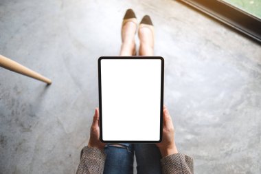 Yerde otururken boş beyaz masaüstü ekranlı tablet bilgisayarını tutan ve kullanan bir kadının en üst görünüm görüntüsü 