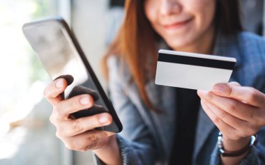 Güzel bir Asyalı kadın cep telefonundan alışveriş yapmak için kredi kartı kullanıyor.
