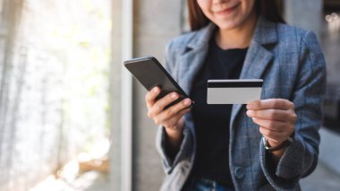 Güzel bir Asyalı kadın cep telefonundan alışveriş yapmak için kredi kartı kullanıyor.