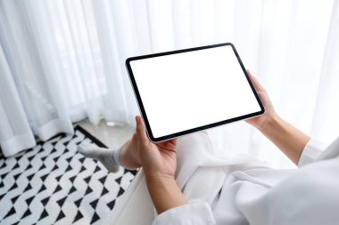 Siyah tabletli, beyaz ekranlı bir kadının sabah rahatlamış bir şekilde yatak odasında otururken görüntüsü.