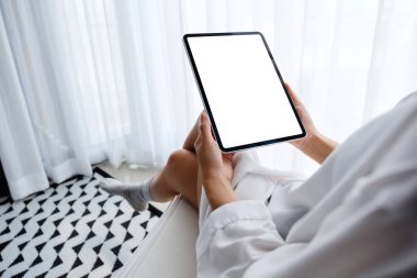 Siyah tabletli, beyaz ekranlı bir kadının sabah rahatlamış bir şekilde yatak odasında otururken görüntüsü.