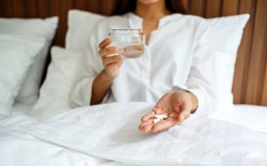 Hasta bir kadının elinde beyaz haplar ve bir bardak su tutarken çekilmiş yakın plan görüntüsü. 