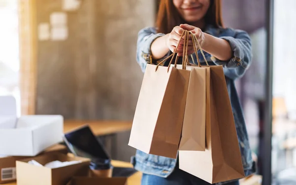 网上购物时 一名妇女拿着购物袋 桌上放着平板电脑和邮筒 展示购物袋的造型 — 图库照片