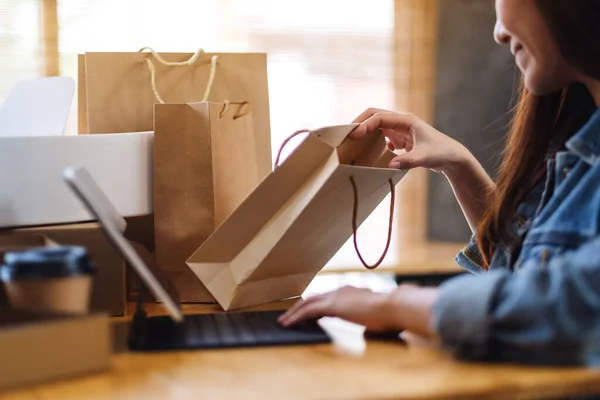 网上购物时使用平板电脑 打开购物袋和桌子上的邮筒的年轻女子的照片 — 图库照片