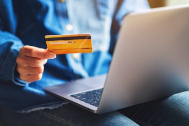 Dizüstü bilgisayar kullanırken kredi kartı tutan bir kadının yakın plan resmi