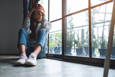 Üzgün ve stresli Asyalı bir kadın odada yalnız oturuyor.