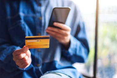 Cep telefonundan alışveriş yapan ve kredi kartı kullanan genç bir kadının yakın plan fotoğrafı.