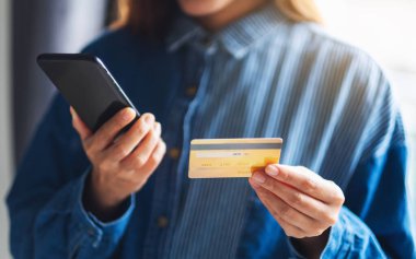 Cep telefonundan alışveriş yapan ve kredi kartı kullanan genç bir kadının yakın plan fotoğrafı.