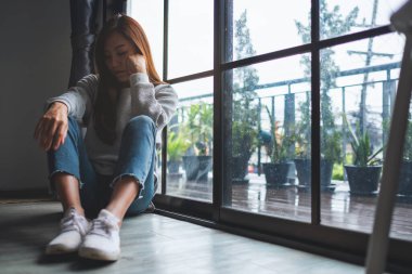 Üzgün ve stresli Asyalı bir kadın odada yalnız oturuyor.