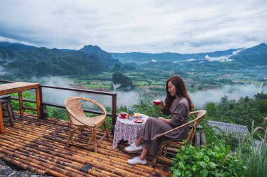 Balkonda sıcak kahve içen güzel bir kadının portresi. Dağlarda ve yeşil arka planda.