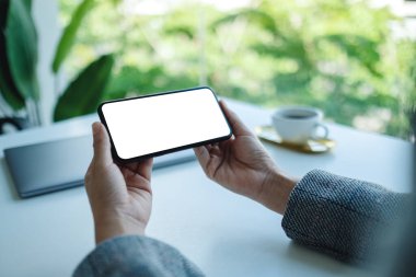 Masasında dizüstü bilgisayarı olan, boş beyaz masaüstü ekranlı cep telefonu tutan bir kadının görüntüsü. 