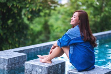 Asyalı güzel bir kadının portre resmi yeşil doğayla iç içe yüzme havuzunda oturmaktan keyif alıyordu.