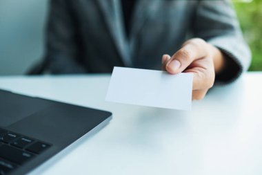 Ofiste dizüstü bilgisayar kullanırken elinde boş kartvizit tutan bir iş kadını.