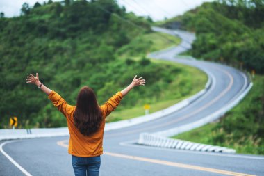 Genç bir kadın yolcunun dikiz görüntüsü. Yüksek dağlardaki eğimli ve dolambaçlı bir yolda açık kollar.