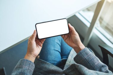Boş beyaz masaüstü ekran ile cep telefonu tutan bir kadının en üst görünüm görüntüsü 