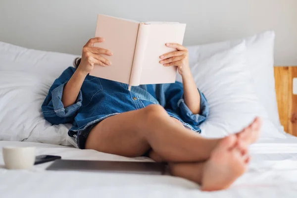 家で白い居心地の良いベッドに横たわっている間に本を読んでいる女性のクローズアップ画像 — ストック写真