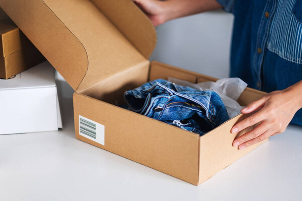 Closeup image of a woman receiving and opening a postal parcel box of clothing at home for delivery and online shopping concept