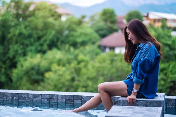 一个年轻美丽的亚洲女人坐在绿树成荫的游泳池旁的画像 — 图库照片
