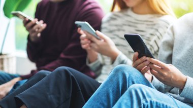 Bir grup genç yan yana otururken cep telefonu kullanıyor ve bakıyor