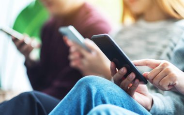 Bir grup genç yan yana otururken cep telefonu kullanıyor ve bakıyor
