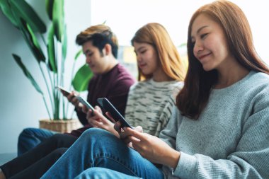 Bir grup genç yan yana otururken cep telefonu kullanıyor ve bakıyor