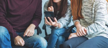 Birlikte otururken aynı cep telefonunu kullanan ve ona bakan bir grup genç.