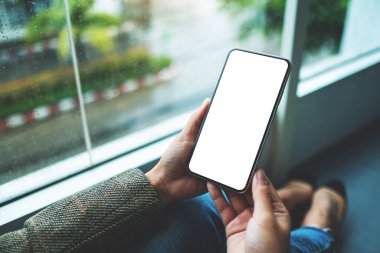 Yerde otururken elinde boş beyaz masaüstü ekran olan cep telefonu tutan bir kadının görüntüsü