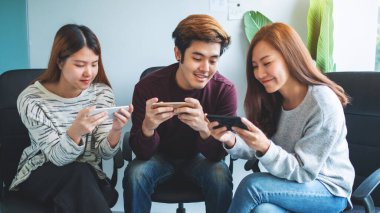 Bir grup genç birlikte otururken cep telefonuyla oyun oynuyor ve kullanıyor