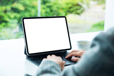 Ofiste bilgisayar bilgisayarı olarak boş beyaz masaüstü ekranı olan tablet klavyesinde yazı yazan ve kullanan bir kadının görüntüsü