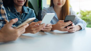 Bir grup genç yan yana otururken cep telefonu kullanıyor ve bakıyor