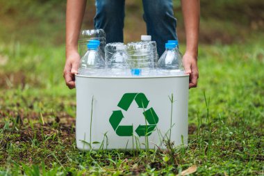 Elinde plastik şişelerle geri dönüşüm kutusunu tutan bir kadın.