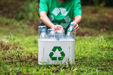 Açık havada plastik şişe toplayıp geri dönüşüm kutusuna koyan bir kadın.