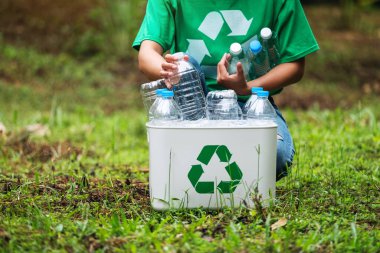 Açık havada plastik şişe toplayıp geri dönüşüm kutusuna koyan bir kadın.