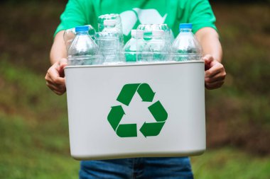 Elinde plastik şişelerle geri dönüşüm kutusunu tutan bir kadın.