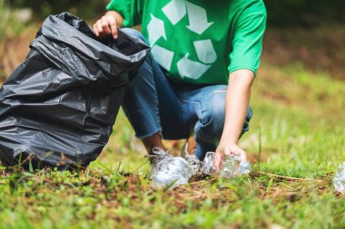 Geri dönüşüm konsepti için parkta plastik bir torbaya çöp şişesi dolduran kadın bir aktivistin yakın plan görüntüsü.