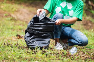 Geri dönüşüm konsepti için parkta plastik bir torbaya çöp şişesi dolduran kadın bir aktivistin yakın plan görüntüsü.