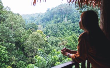 Balkonda duran ve güzel yeşil bir dağ manzarasına bakan güzel bir kadın gezginin dikiz görüntüsü.