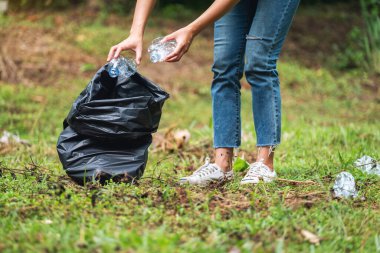 Geri dönüşüm konsepti için parkta plastik bir torbaya çöp şişesi dolduran kadın bir aktivistin yakın plan görüntüsü.